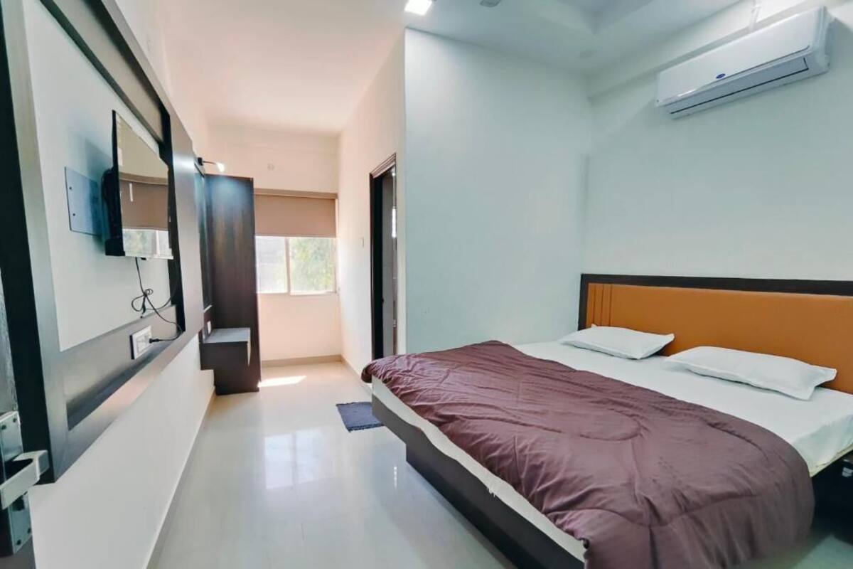 A bedroom with a bed, a mirror, an air conditioner, and a door leading to another room.