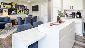 A modern kitchen with white cabinets, a marble countertop, and a coffee station.