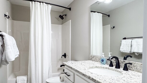 A bathroom with a shower curtain, a toilet, a sink with a mirror, and a towel rack.