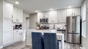 A modern kitchen with white cabinets, a stainless steel refrigerator, and a central island with two blue chairs.