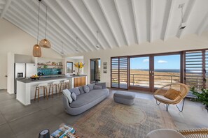 Ein moderner Wohnraum mit einer Küche, einem großen grauen Sofa und Blick auf den Strand.