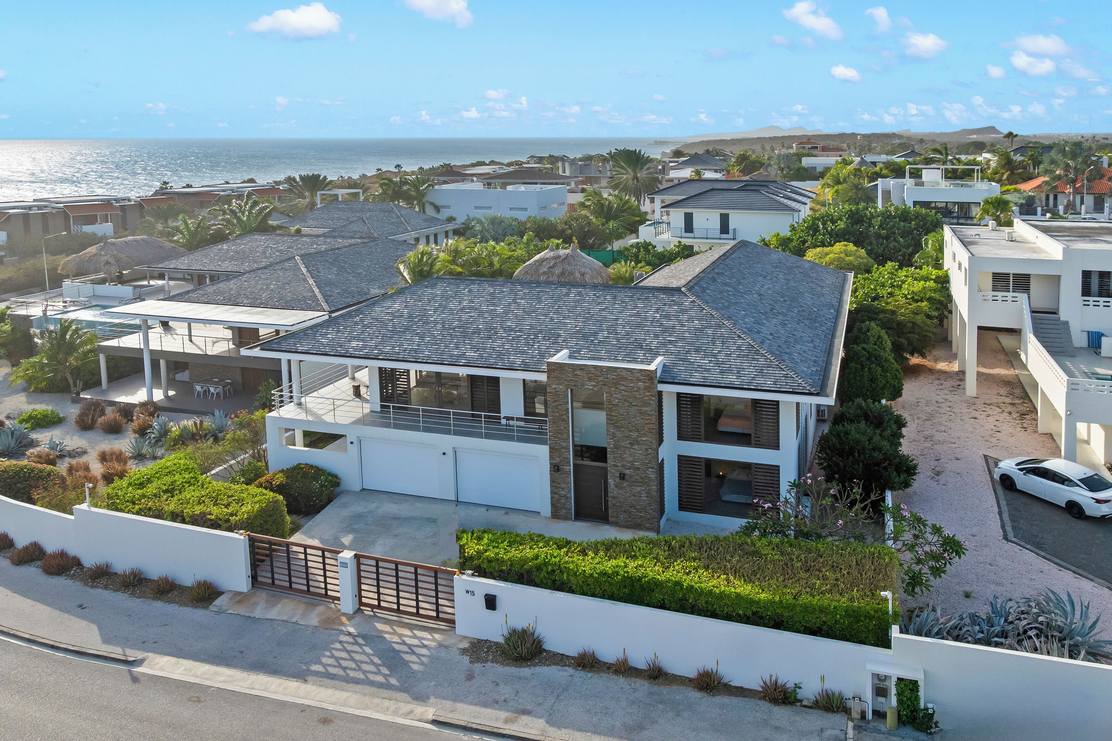 Een modern huis met twee verdiepingen en een grote garage, omgeven door weelderig groen en uitzicht op de oceaan.