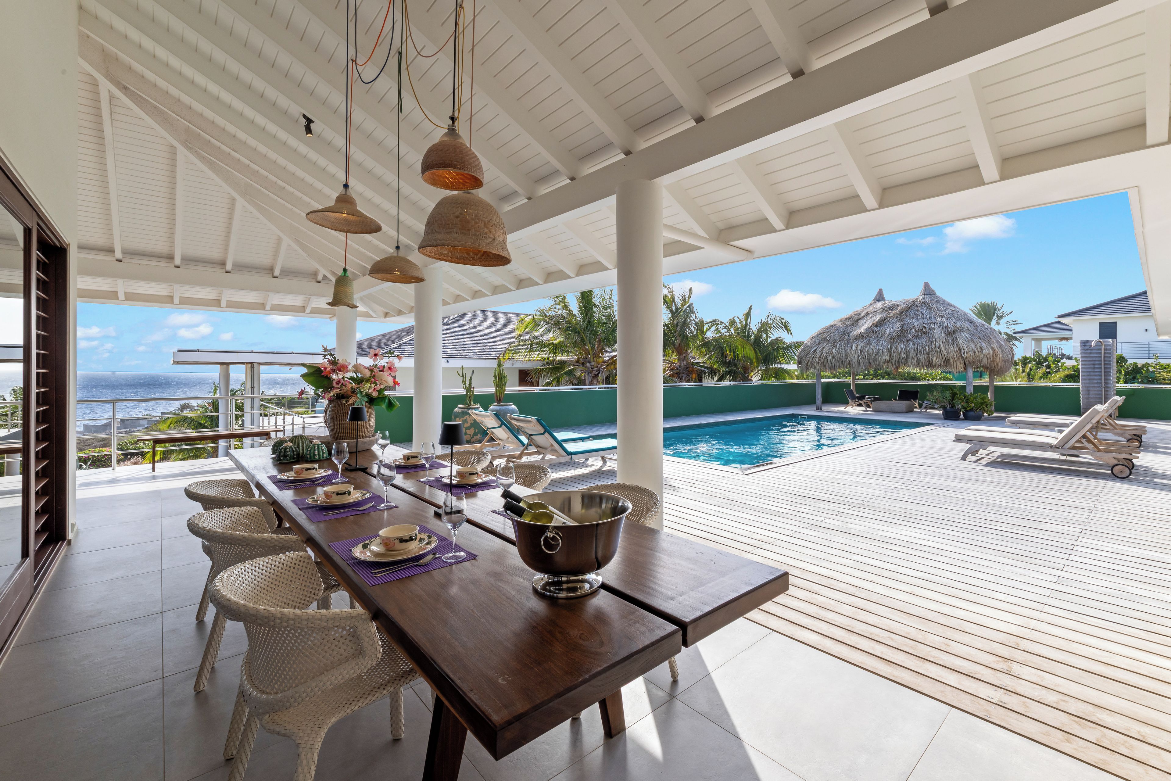 A covered outdoor dining area with a view of a pool and ocean.