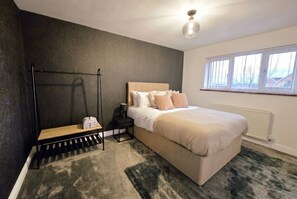 Ein Schlafzimmer mit Bett, Nachttisch, Lampe, Bank und einem Fenster.