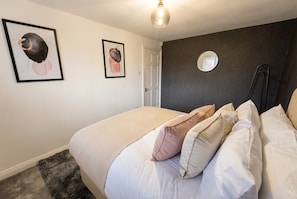 A bedroom with a bed, pillows, a framed artwork, a door, and a mirror on the wall.