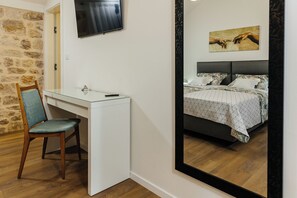 Un dormitorio con cama, escritorio, silla, televisión y un cuadro en la pared.