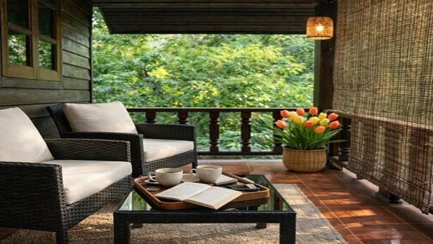A wicker sofa with cushions, a glass coffee table with a book and cups, and a potted plant with tulips on a balcony with a view of greenery. - Tropical Home for Remote Work & Long Stays | Hin Kong (Ko Pha-ngan)
