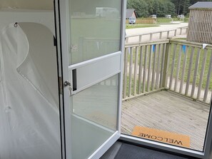 A glass door with a metal handle, a welcome mat, and a wooden deck with a railing. - Sherwood Pines - Geodome (Mansfield)