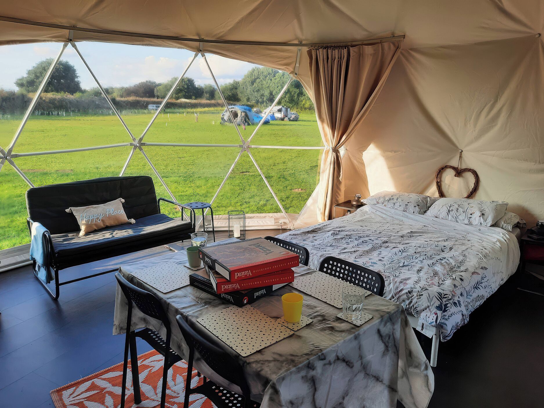Alojamiento con tienda de campaña, que incluye una cama, un sofá, una mesa con libros y una taza, y vistas al exterior.