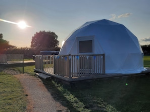 A dome-shaped tent with a small door and a window, surrounded by a wooden deck and a fence. - Sherwood Pines - Geodome (Mansfield)