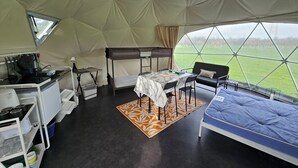 Een tent met een stapelbed, een tafel met stoelen, een kleine kitchenette en uitzicht op de omgeving.