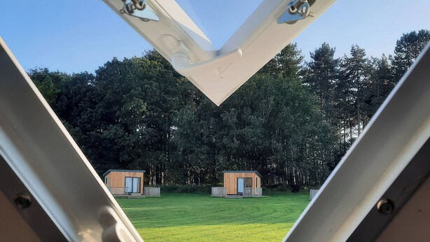 Een uitzicht door een drielingsraam op een grasveld met twee kleine houten hutjes.
