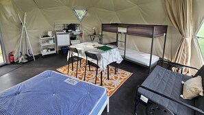 Een tentaccommodatie met stapelbedden, een bureau met stoel, een klein tafeltje en een bank.