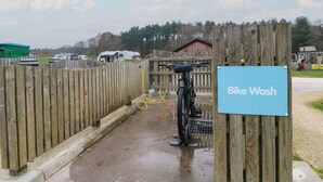 Een houten hek, een fietswasstation en een bord met de tekst 'Fietswas'.