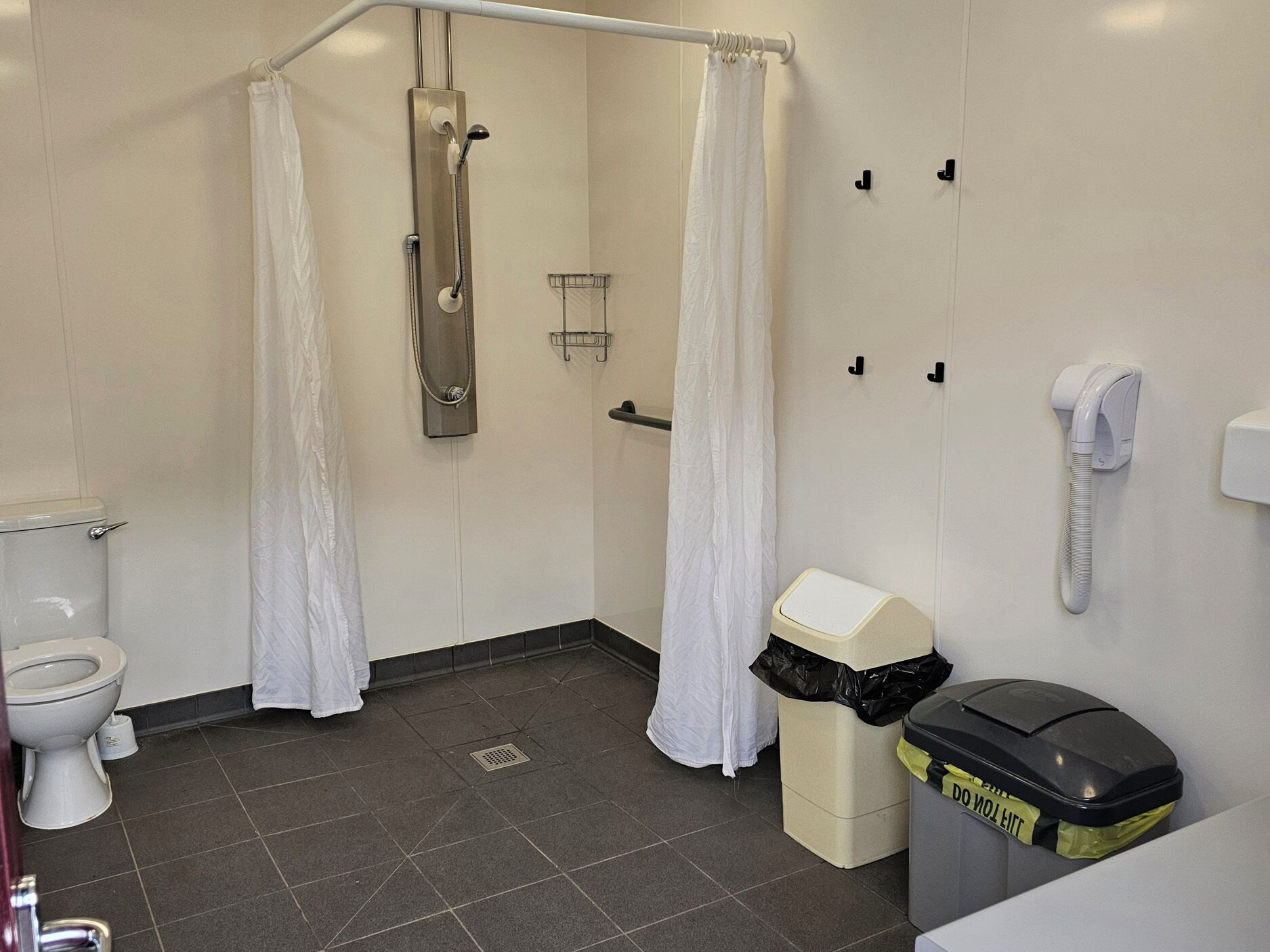 A bathroom with a shower, toilet, and a trash bin.