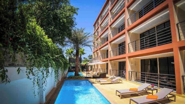 Et hotel med swimmingpool, liggestole og en bygning med flere etager.