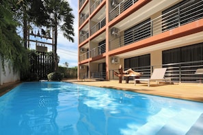 A swimming pool with lounge chairs and a building with balconies. - 1BR Mountain View Apartment Rawai | CapitalPro (Rawai)