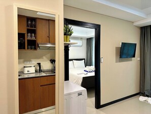 A hotel room with a kitchenette, a bed, a TV, and a bathroom. - 1BR Apartment Pool Rawai Beach Capital Pro (Rawai)