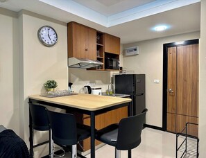 A compact kitchen with wooden cabinets, a microwave, a refrigerator, a clock, and a small plant. - 1BR Apartment Pool Rawai Beach Capital Pro (Rawai)