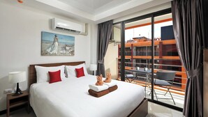 Hotelkamer met een groot bed, een schilderij aan de muur, een airconditioning, een balkon met stoelen en tafels, en uitzicht op gebouwen.