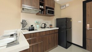 Een keuken met houten kastjes, een magnetron, een zwarte koelkast, een spoelbak en een klok aan de muur.