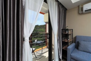 A balcony with a table and chairs, a blue sofa, and a bookshelf. - 1BR Apartment in Nai Harn Condo | CapitalPro (Rawai)