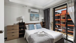 Moderni hotellihuone, jossa on sänky, työpöytä, tuoli, ikkuna verhoineen ja näkymä oranssiin rakennukseen.