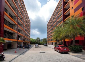 A multi-story parking garage with a MiniMarket on the ground floor, surrounded by palm trees and parked cars. - 1BR Apartment in Nai Harn Condo | CapitalPro (Rawai)