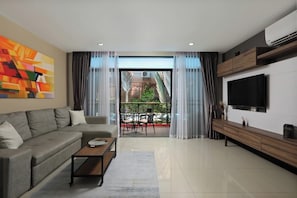 Ein modernes Wohnzimmer mit Sofa, Couchtisch, Fernseher und einem Balkon mit Gartenmöbeln.