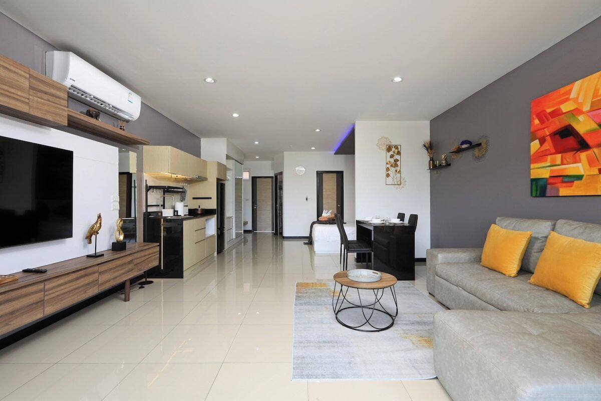 A modern living room with a flat-screen TV, a sofa, a coffee table, and a dining area with chairs.
