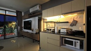 A modern kitchen with built-in appliances, a TV, and a dining area with a bench. - Spacious Studio Naiharn Beach Condo | CapitalPro (Rawai)
