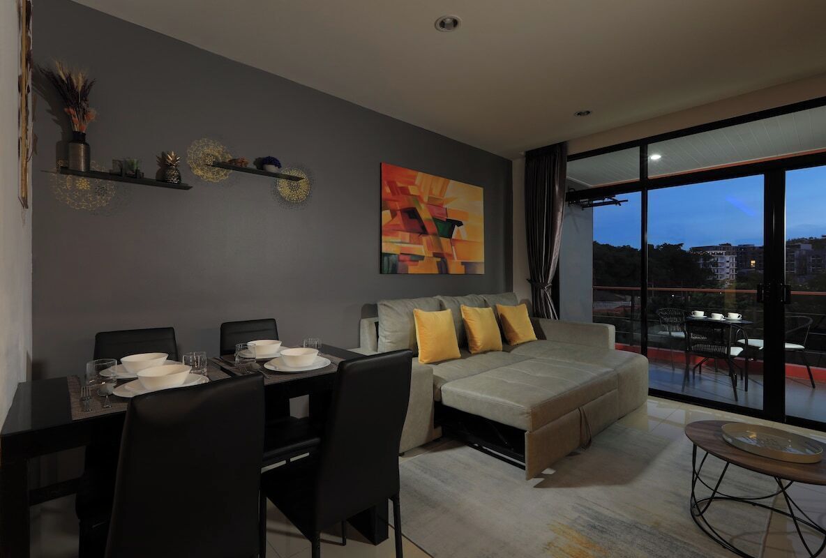 A modern living room with a sofa, dining table, and chairs. There is a large window with a view of the city.