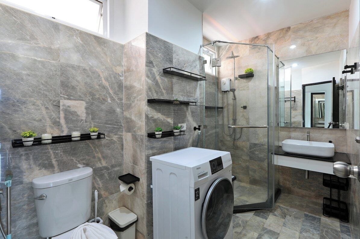 Une salle de bain moderne dotée d’une douche à parois de verre, d’un lave-linge encastré, de toilettes et d’un lavabo.