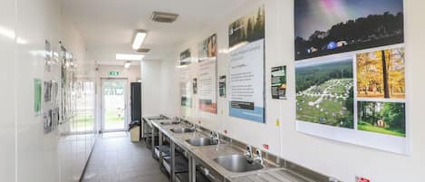 A clean, well-lit public restroom with multiple sinks and hand dryers, and informational posters on the walls.