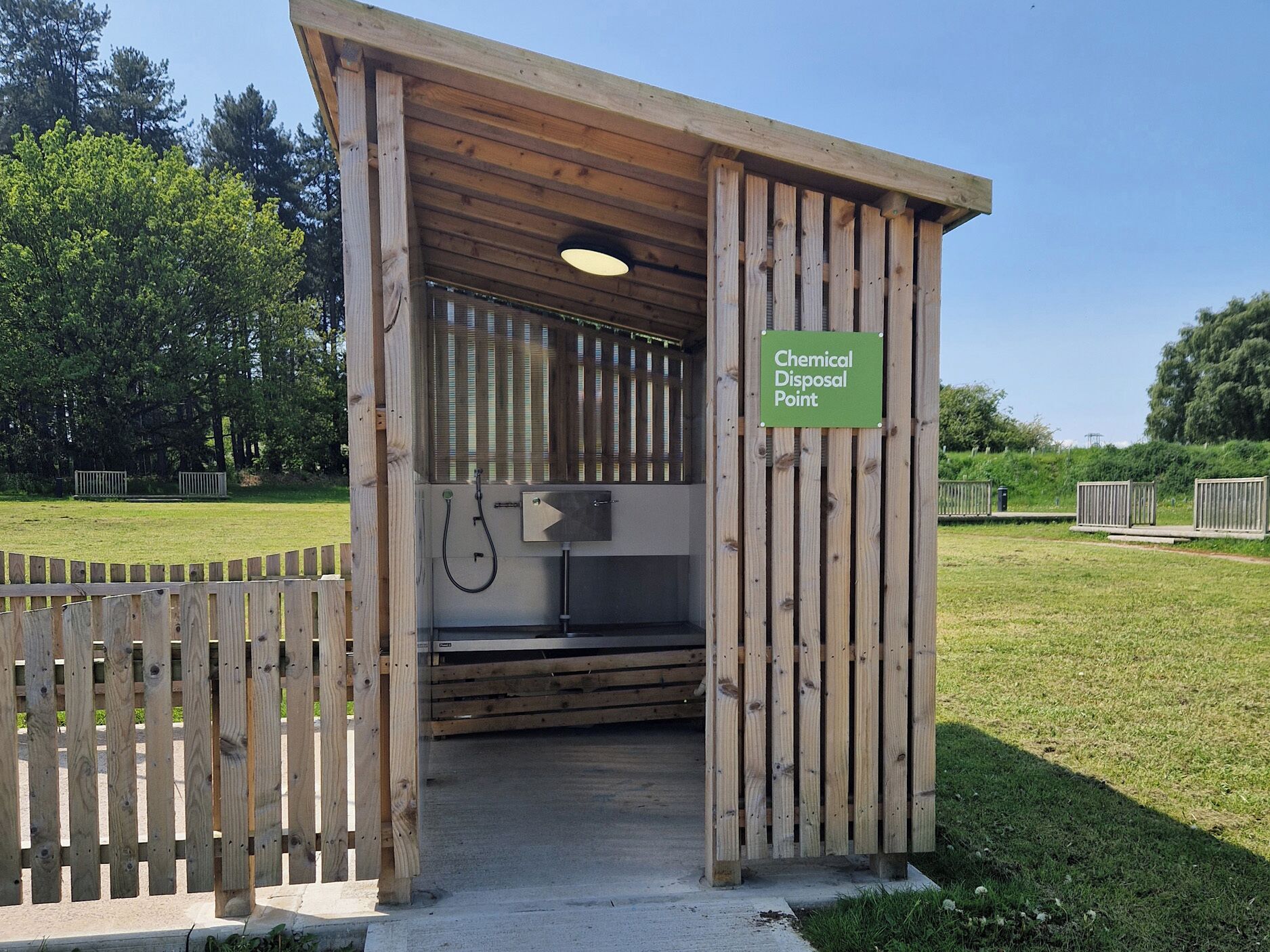 A wooden structure labeled as a Chemical Disposal Point with a hose and a metal box.
