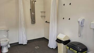 A bathroom with a shower, toilet, and a trash bin.
