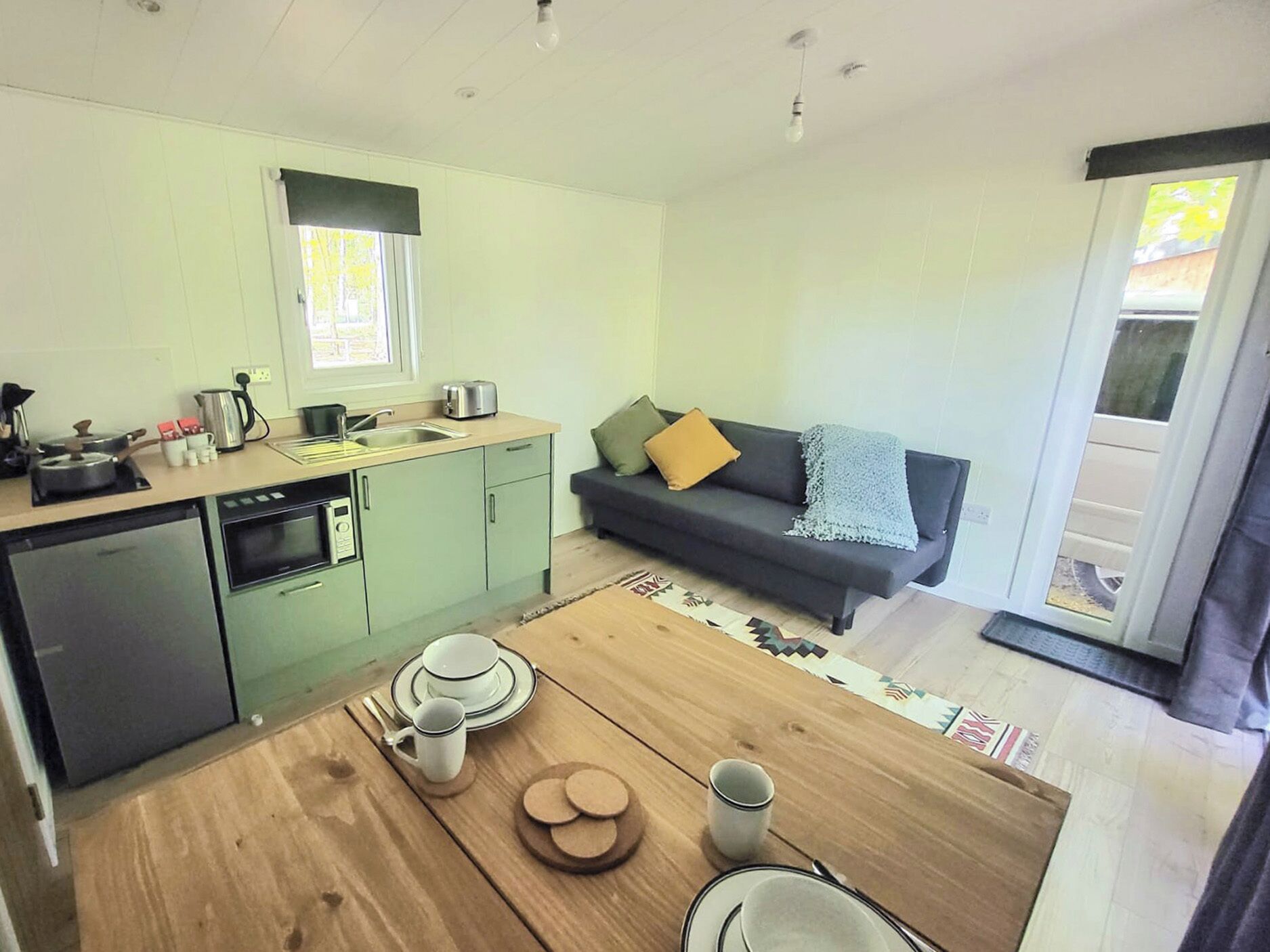 Cocina compacta con comedor, sofá y puerta corredera de cristal.