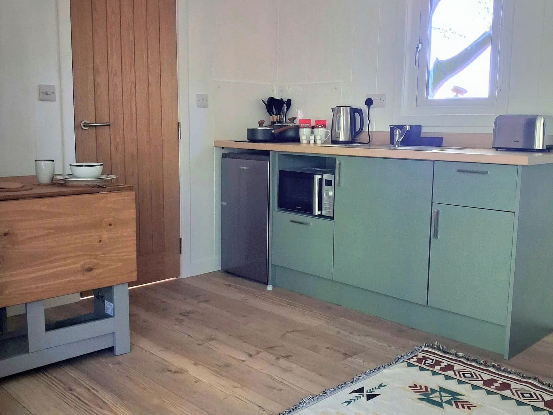 A compact kitchen with a microwave, kettle, and a small refrigerator.