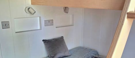 A compact RV interior with a bunk bed, a small seating area with a cushion, and a window.