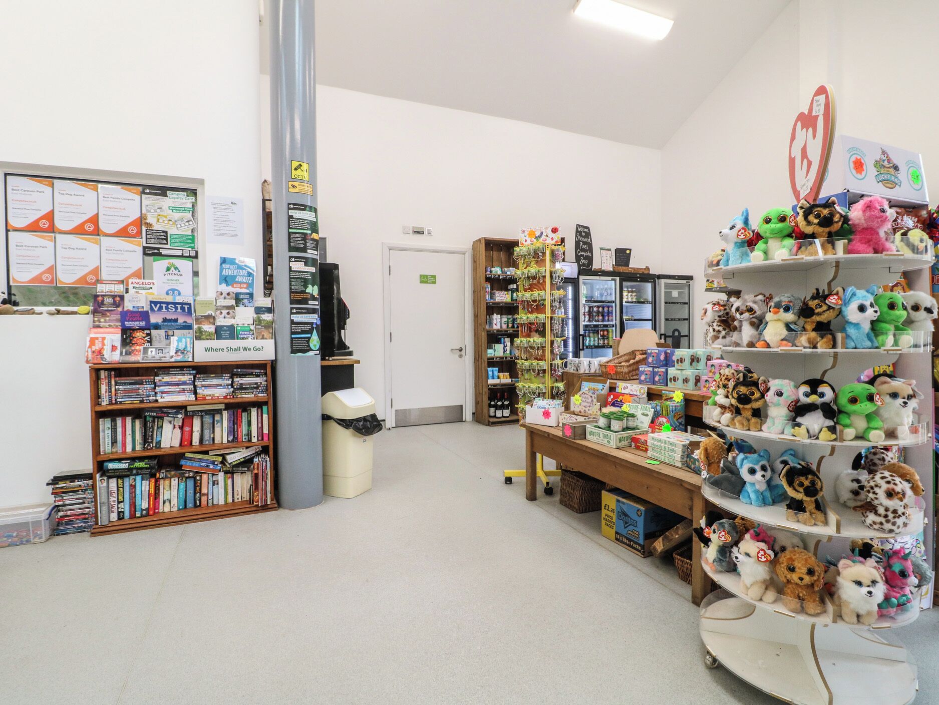 Una biblioteca con estanterías, una máquina de café, un cubo de basura y un estante con peluches.