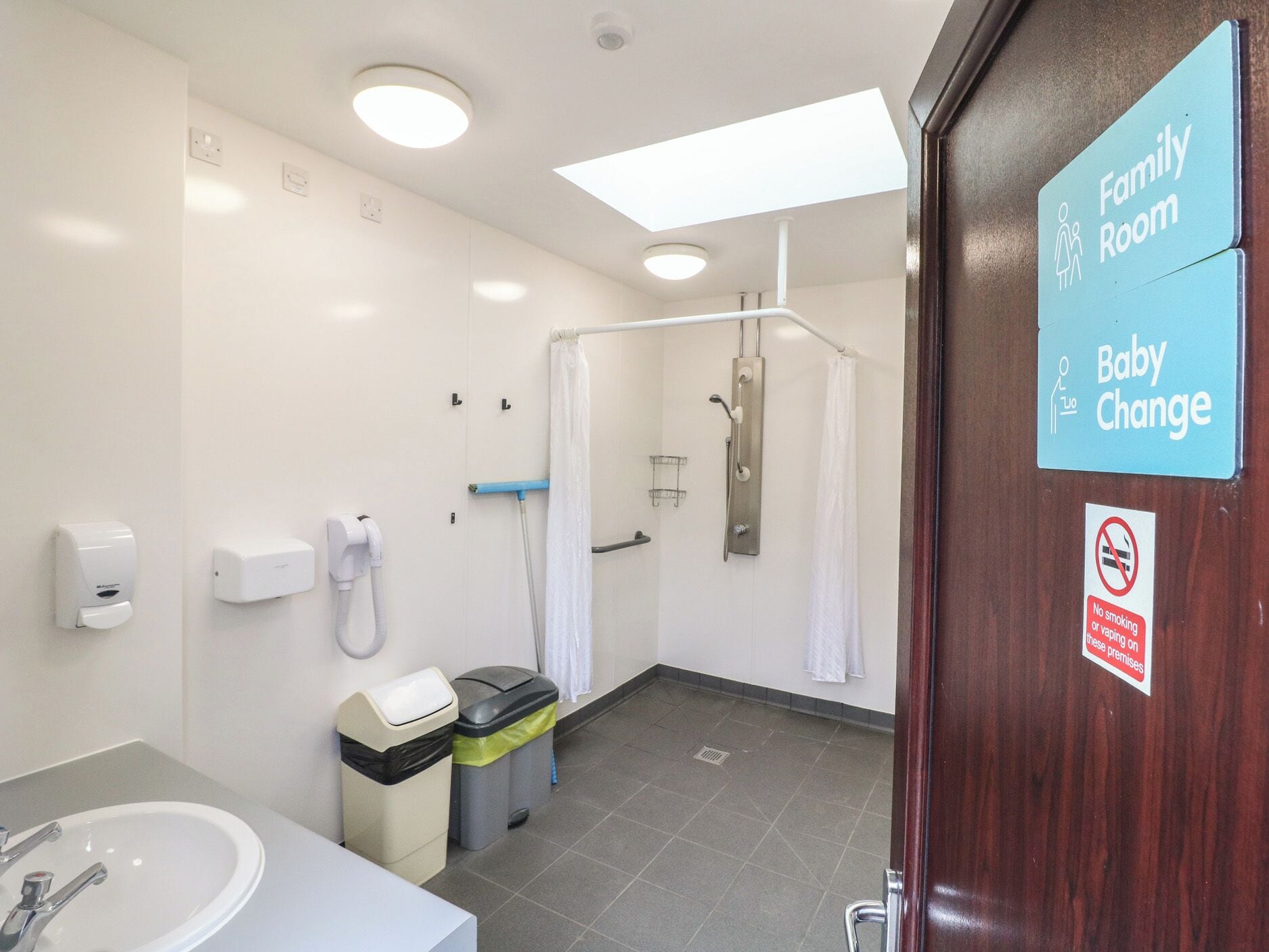 A family room with a baby changing area, a shower, and a sink with hand dryers.