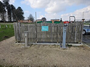 Ein Holzzaun mit einem Schild, das Fahrradreparaturen anzeigt, ein Fahrradständer aus Metall und ein Kiesgrund.