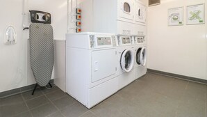 Uma lavanderia com máquina de lavar e secadora empilhadas, tábua de passar e painel de controle fixado na parede.