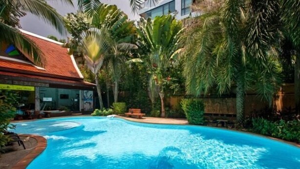 A swimming pool surrounded by lush greenery and a building with a red roof. - 1BR Mountain View Nai Harn Beach | Capital Pro (Rawai)