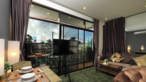 A modern living room with a dining area, large windows, and a flat-screen TV. - 1BR Mountain View Nai Harn Beach | Capital Pro (Rawai)