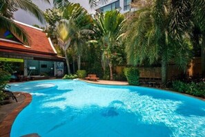 A swimming pool surrounded by tropical plants and a building with a red roof. - 1BR Mountain view Apartment Naiyang | Capital Pro (Rawai)