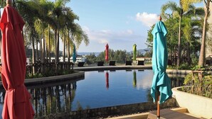 A pool area with lounge chairs and umbrellas, surrounded by palm trees and a clear sky. - 1BR Mountain View Apartment Surin | CapitalPro (Surin)