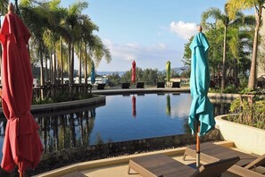 A pool area with lounge chairs and umbrellas, surrounded by palm trees and a clear sky. - 1BR Mountain View Apartment Surin | CapitalPro (Surin)