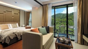 A hotel room with a bed, sofa, balcony with a table, and a view of greenery. - 1BR Mountain View Apartment Surin | CapitalPro (Surin)