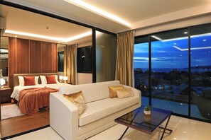 Ein modernes Hotelzimmer mit einem großen Bett, einer Sitzecke, einem Glastisch und Blick auf die Stadt durch große Fenster.